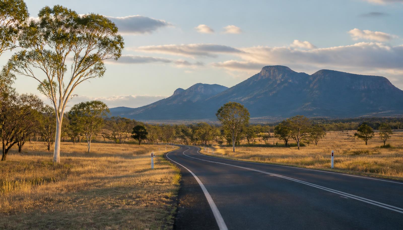 Open Queensland highway curving toward a distant range at golden hour